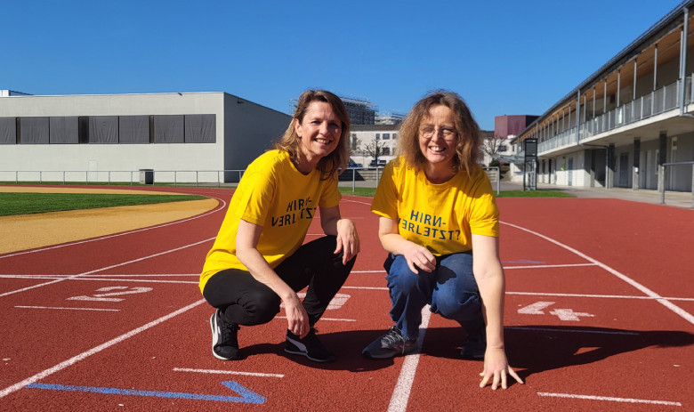 Zwei Frauen mit gelben FRAGILE-T-Shirts kauern auf der Laufbahn.
